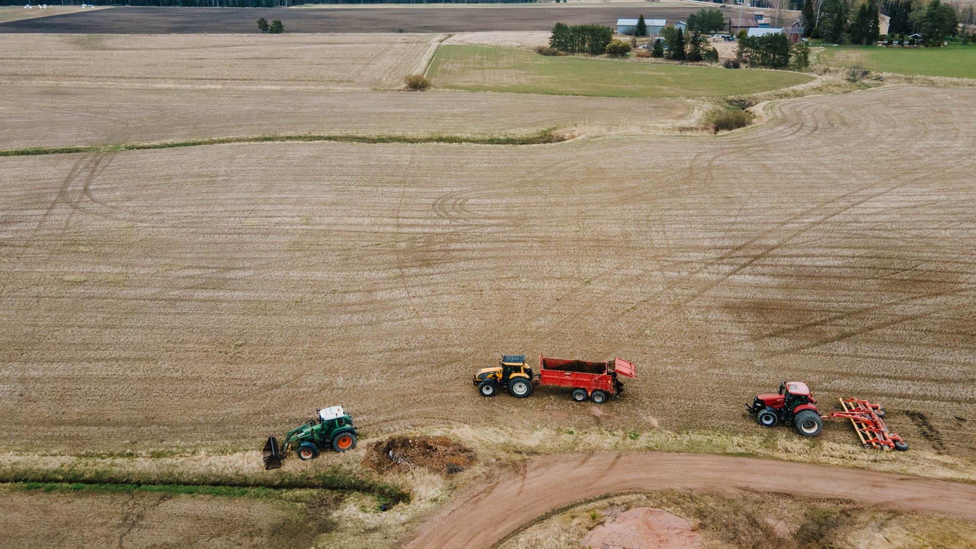 Kolme traktoria peltotöissä maalaismaisemassa