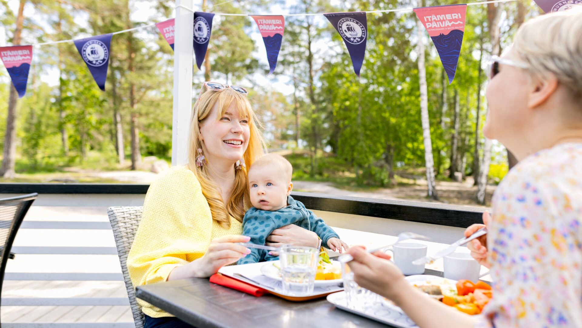 Kaksi naista ja lapsi syömässä Itämeripäivän lounasta ulkona terassilla