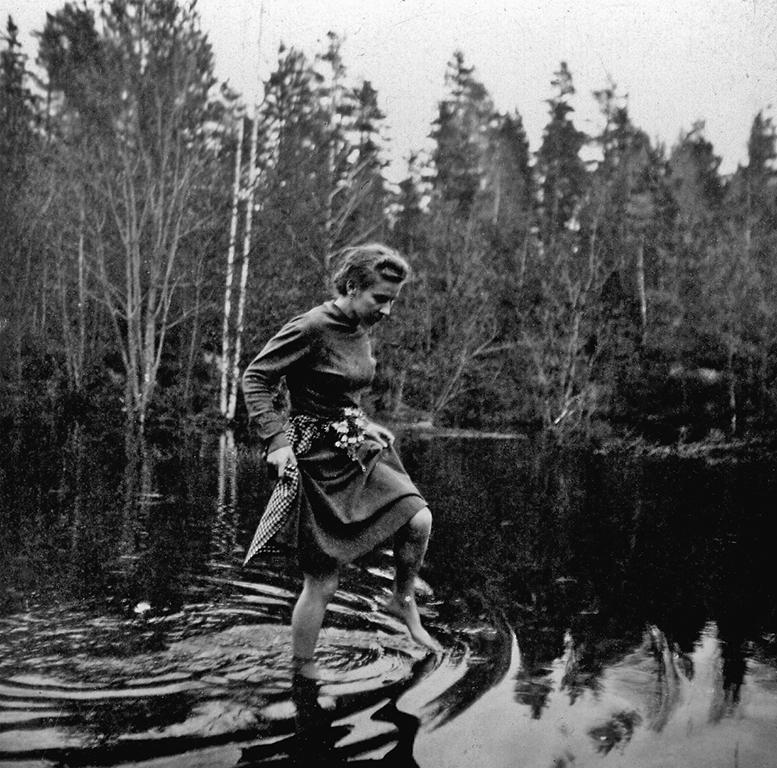 Nuori Tove Jansson kävelee vedessä helmojaan nostaen