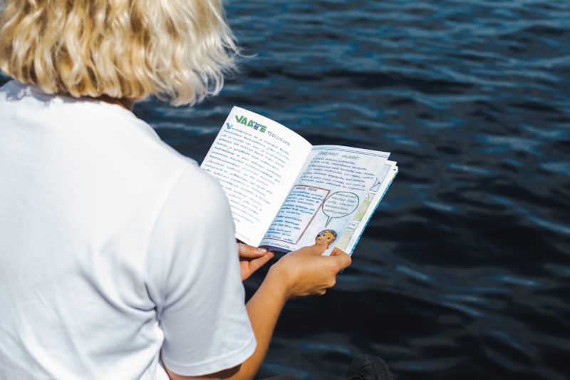 Nainen lukee Vihreät Sanomat -lehteä meren äärellä.