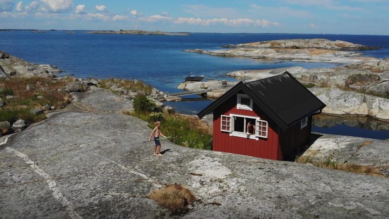 Punainen mökki saaristossa ja lapsi kalliolla onkivapa käsissään