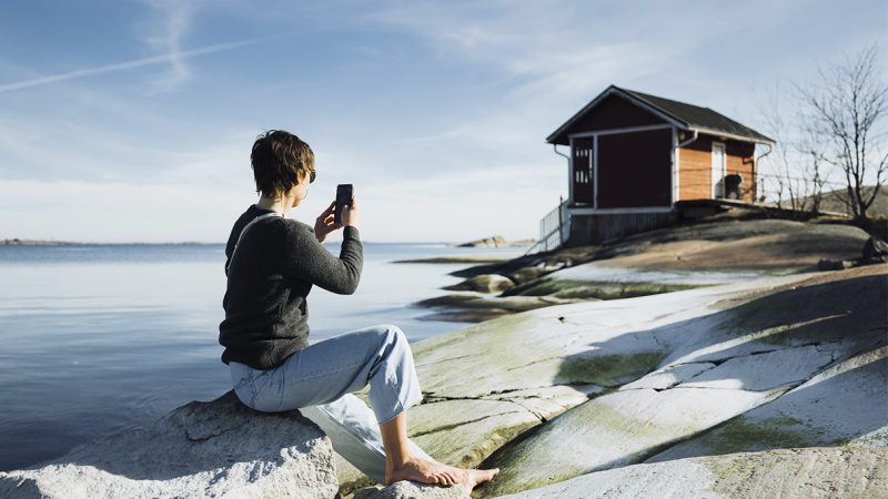 nainen istuu meren rannalla puhelin kädessä