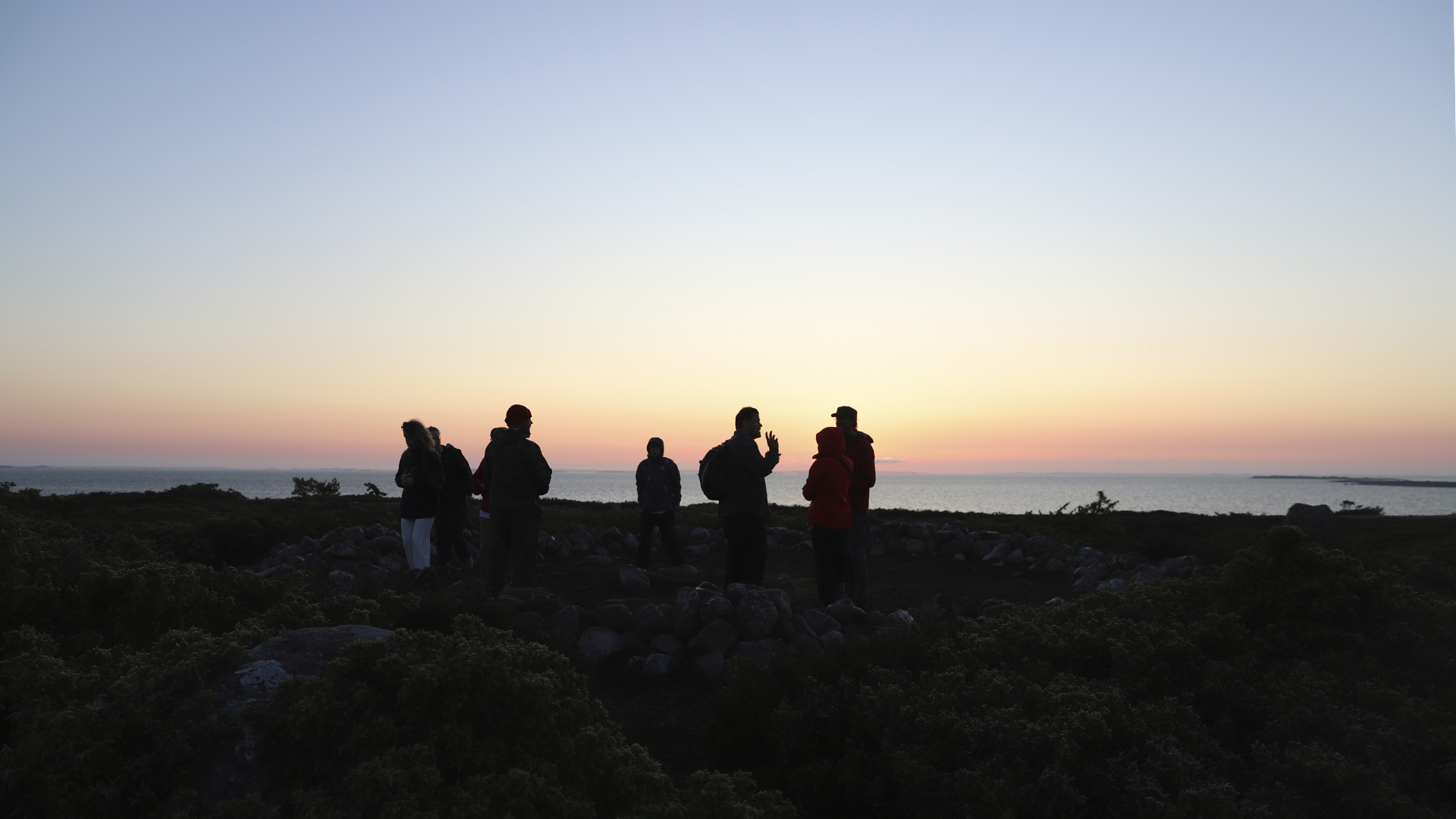 ihmisiä katsomassa auringonnousua rantakalliolla