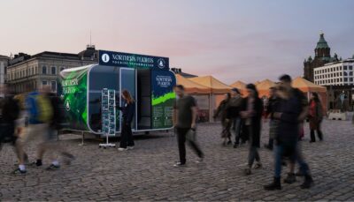 nainen katselee postikortteja infokioskin edessä