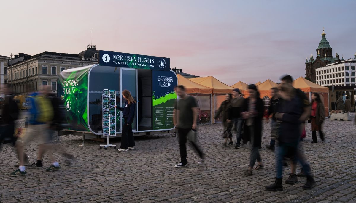 nainen katselee postikortteja infokioskin edessä