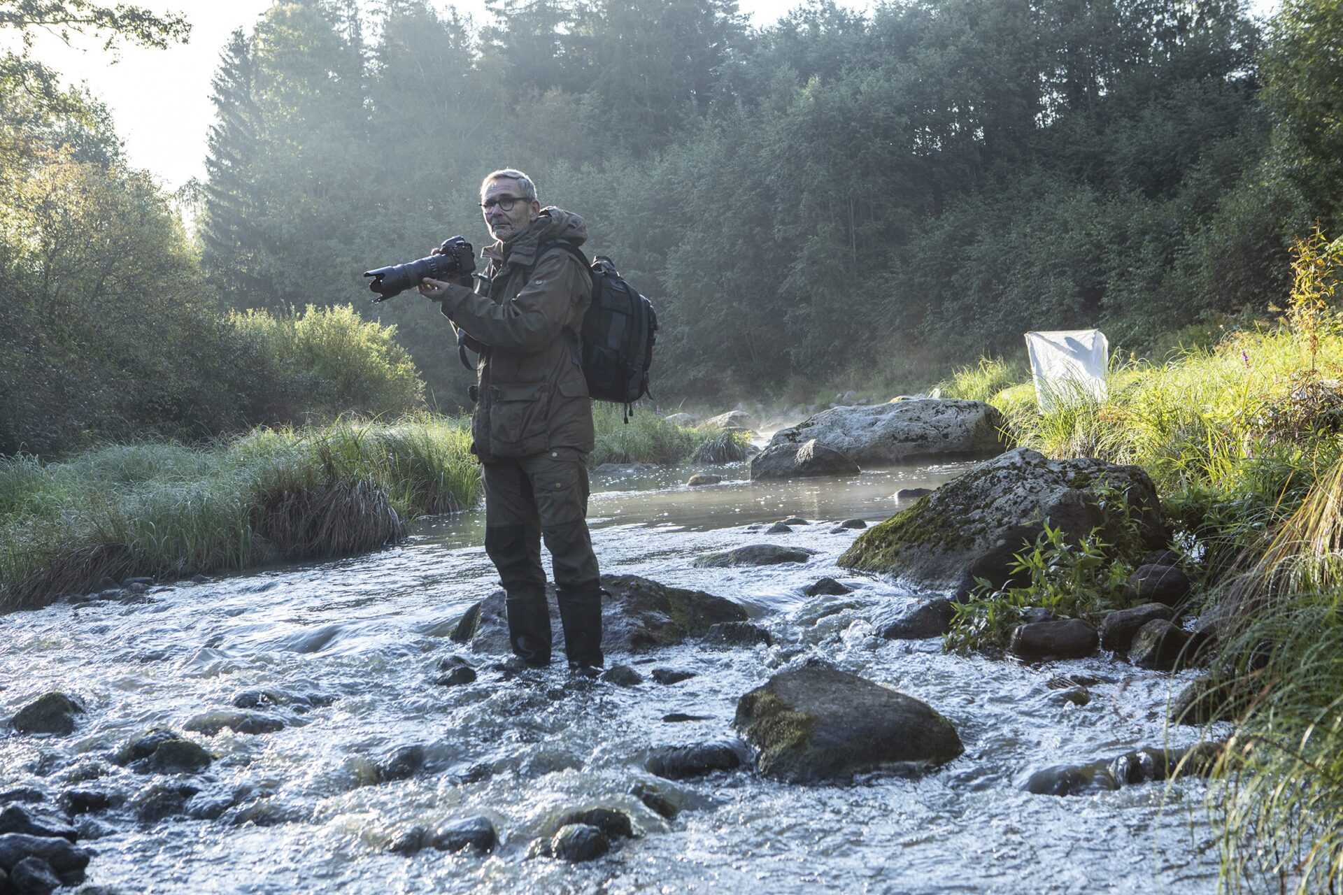Mies kameran kanssa seisomassa keskellä jokea.